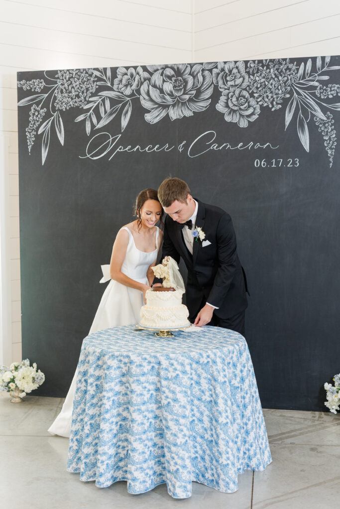 Custom chalkboard wedding sign backdrop as bride and groom cut wedding cake